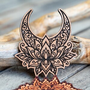 May include: A laser-cut wooden crescent moon and lotus flower design. The intricate details are burned into the wood, creating a dark brown contrast against the natural wood grain. The design is likely a decorative element or craft supply.