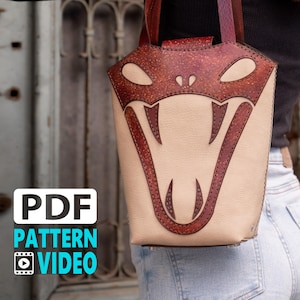 Può includere: Una borsa a mano in pelle marrone con un design a testa di serpente. La borsa ha una chiusura a lembo e un manico superiore. La borsa viene indossata da una persona.