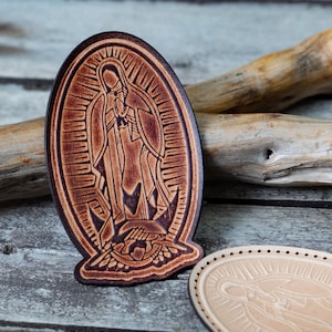 Op de afbeelding: Twee ovale leren patches met een gegraveerd beeld van de Maagd Maria. De patch links is bruin en de patch rechts is lichtbruin.