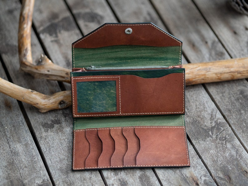 May include: A brown leather wallet with a green leather interior. The wallet is open and has multiple card slots and a zippered compartment.