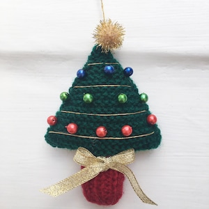 Könnte beinhalten: Handgefertigter Weihnachtsbaumschmuck. Der grüne gehäkelte Baum ist mit bunten Perlen und Goldfaden verziert. Ein roter Topf und ein goldenes Band bilden die Basis. Oben befinden sich eine goldene Schlaufe und ein Bommel. Festliche Weihnachtsdekoration.