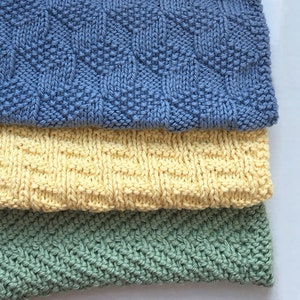 Puede incluir: Tres paños de cocina de punto en diferentes colores y patrones. El paño de cocina superior es azul con un patrón geométrico, el paño de cocina del medio es amarillo con un patrón tejido y el paño de cocina inferior es verde con un patrón de espiga.