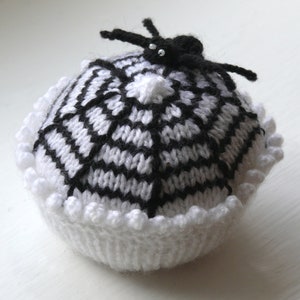 May include: A white knitted spiderweb with a black spider on top. The web has a white crocheted border.