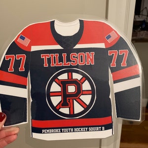 May include: A navy blue and red hockey jersey cutout with the name "TILLSON" and the number "77" in white. The jersey features a circular logo with a "P" and the text "PEMBROKE YOUTH HOCKEY SQUIRT B". American flags are on the shoulders.