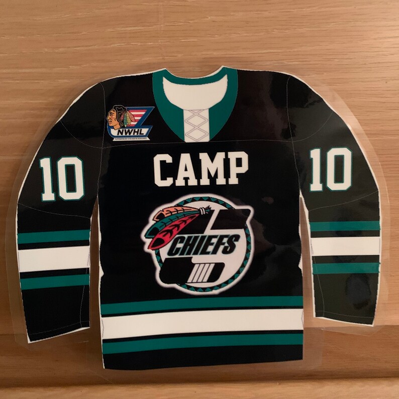 May include: A black and teal hockey jersey-shaped sticker with the word "CAMP" in white block letters. The jersey features the number "10" on both sleeves and a Chiefs logo. The NWHL logo is visible on the upper left.