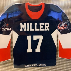 May include: A navy blue hockey jersey with white and red accents. The jersey features the name "MILLER" and the number "17" in white block letters. The team logo and "CCYHA BLUE JACKETS" are also visible.
