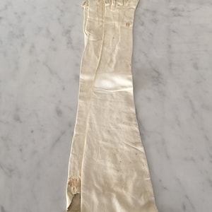 May include: A pair of long, white leather gloves. The gloves are folded in half and have a slight yellowing from age.