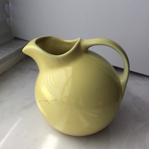 Op de afbeelding: Een gele keramische kan met een rond lichaam en een handvat. De kan is gemaakt van glad, glanzend materiaal.