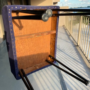 May include: The underside of a blue upholstered stool with black metal legs. The stool is made of wood and has a simple design.