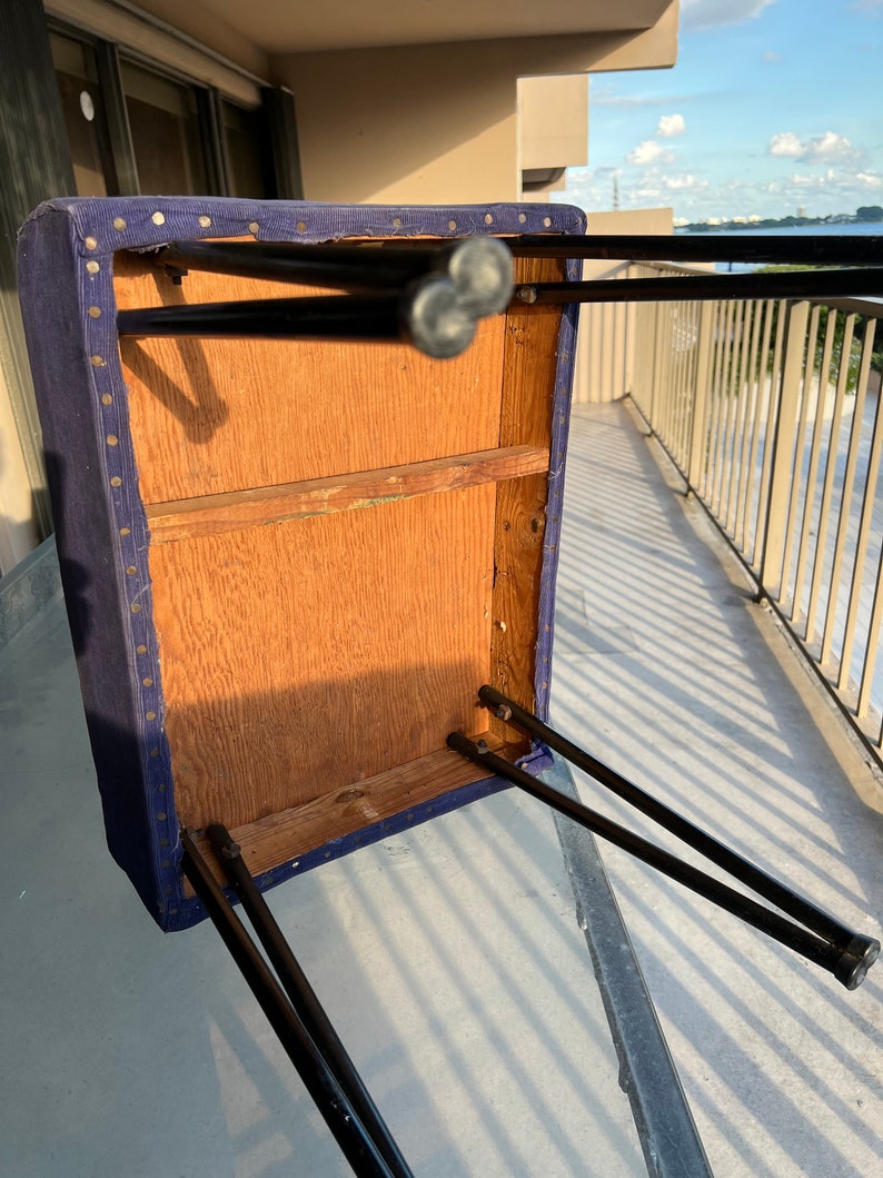 May include: The underside of a blue upholstered stool with black metal legs. The stool is made of wood and has a simple design.