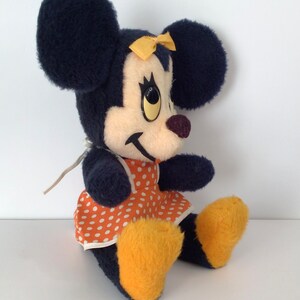Może przedstawiać: Pluszowa zabawka przedstawiająca Minnie Mouse, dziewczynę Myszki Miki. Ma na sobie czerwoną sukienkę w białe kropki z ż&oacute;łtą kokardką. Ma duże czarne uszy i ż&oacute;łte buty.