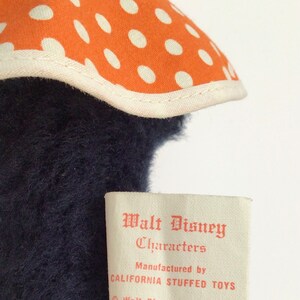 Może przedstawiać: Etykieta vintage pluszowej zabawki Walt Disney Characters z pomarańczowymi kropkami i tekstem "Walt Disney Characters, Manufactured by California Stuffed Toys, &copy; Walt Disney Productions".