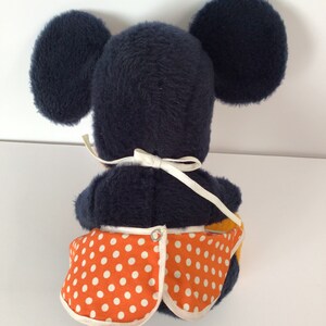 Może przedstawiać: Pluszowa zabawka Mickey Mouse w niebieskiej sukience w białe kropki. Zabawka siedzi na białym tle.