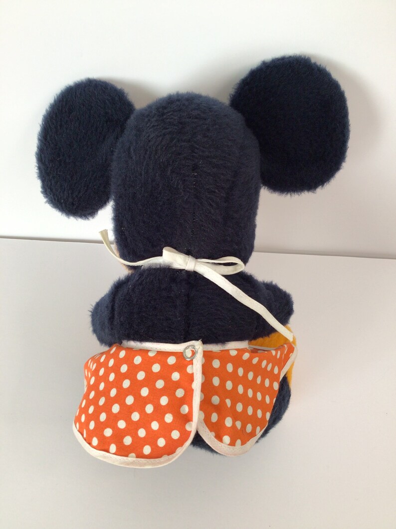 Może przedstawiać: Pluszowa zabawka Mickey Mouse w niebieskiej sukience w białe kropki. Zabawka siedzi na białym tle.