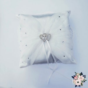 May include: White satin ring pillow with a tulle overlay and a silver double heart embellishment with rhinestones. The pillow has a white satin ribbon.