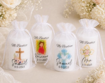 May include: Four white pillar candles wrapped in sheer white organza drawstring bags. Each candle features a unique religious graphic, including crosses and a figure, with the text Mi Bautizo or My Baptism, names, and dates printed on the front.