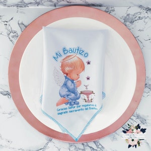 Op de afbeelding: Een witte servet met blauwe bies heeft een blauwe en witte illustratie van een engel met de tekst "Mi Bautizo" en "Gracias Señor por regalarme el sagrado sacramento del Bautizo".