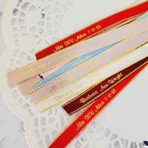 May include: Assorted satin ribbons in red, pink, blue, and burgundy, with gold trim and personalized text. The ribbons feature phrases like "Mis XV A&ntilde;os" and names with dates, ideal for event favors or decorations.