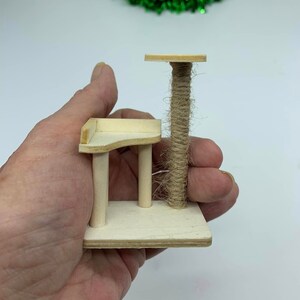 May include: A miniature wooden cat tree with a sisal-covered scratching post and two platforms. The cat tree is small enough to fit in the palm of a hand.