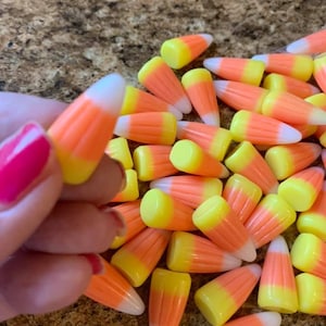 Puede incluir: Primer plano de un mont&oacute;n de caramelos de ma&iacute;z. Los caramelos son de color naranja, amarillo y blanco, con forma triangular. Una mano con esmalte de u&ntilde;as rosa sostiene una pieza.