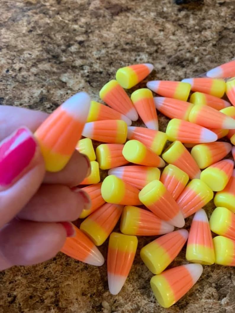 Puede incluir: Primer plano de un mont&oacute;n de caramelos de ma&iacute;z. Los caramelos son de color naranja, amarillo y blanco, con forma triangular. Una mano con esmalte de u&ntilde;as rosa sostiene una pieza.