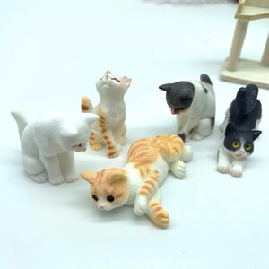 May include: Five miniature ceramic cat figurines in various poses. The cats are white, black and white, orange and white, and gray and white. The figurines are perfect for a miniature dollhouse or fairy garden.