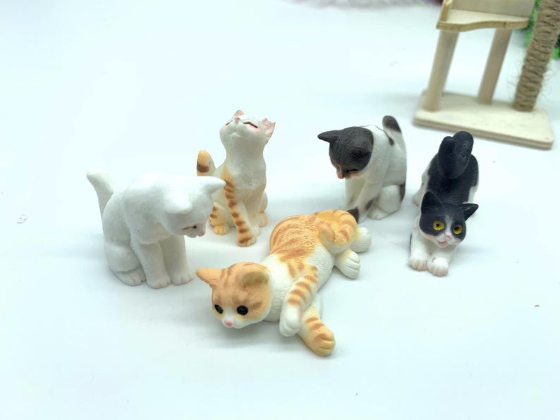 May include: Five miniature ceramic cat figurines in various poses. The cats are white, black and white, orange and white, and gray and white. The figurines are perfect for a miniature dollhouse or fairy garden.