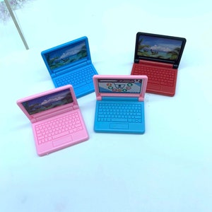 Puede incluir: Cuatro ordenadores port&aacute;tiles de juguete en diferentes colores: rosa, azul, azul claro y rojo. Cada ordenador port&aacute;til tiene una pantalla con una escena de playa y un teclado.