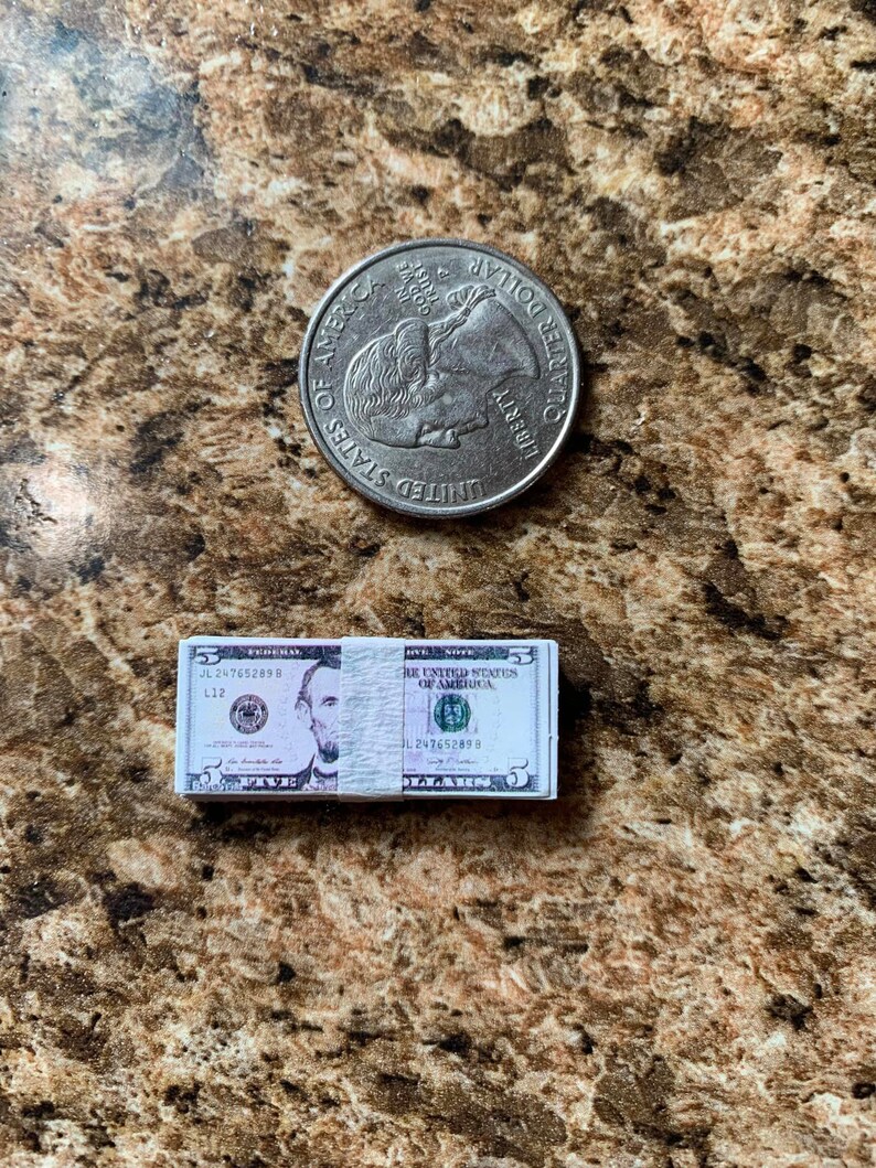 Może przedstawiać: Stos pięciu banknot&oacute;w dolara amerykańskiego z portretem Abrahama Lincolna z przodu i pomnikiem Lincolna z tyłu. Banknoty są złożone na p&oacute;ł i mają numer seryjny JL 247652898.