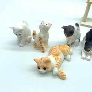 May include: Five miniature ceramic cat figurines in various poses. The cats are white, black, orange, and brown with black markings.