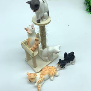 May include: A set of four miniature cat figurines, including a white cat with black spots, a black cat with white spots, a white cat with orange spots, and an orange cat with white spots. The cats are posed in various playful positions, including one cat climbing a miniature cat tree.