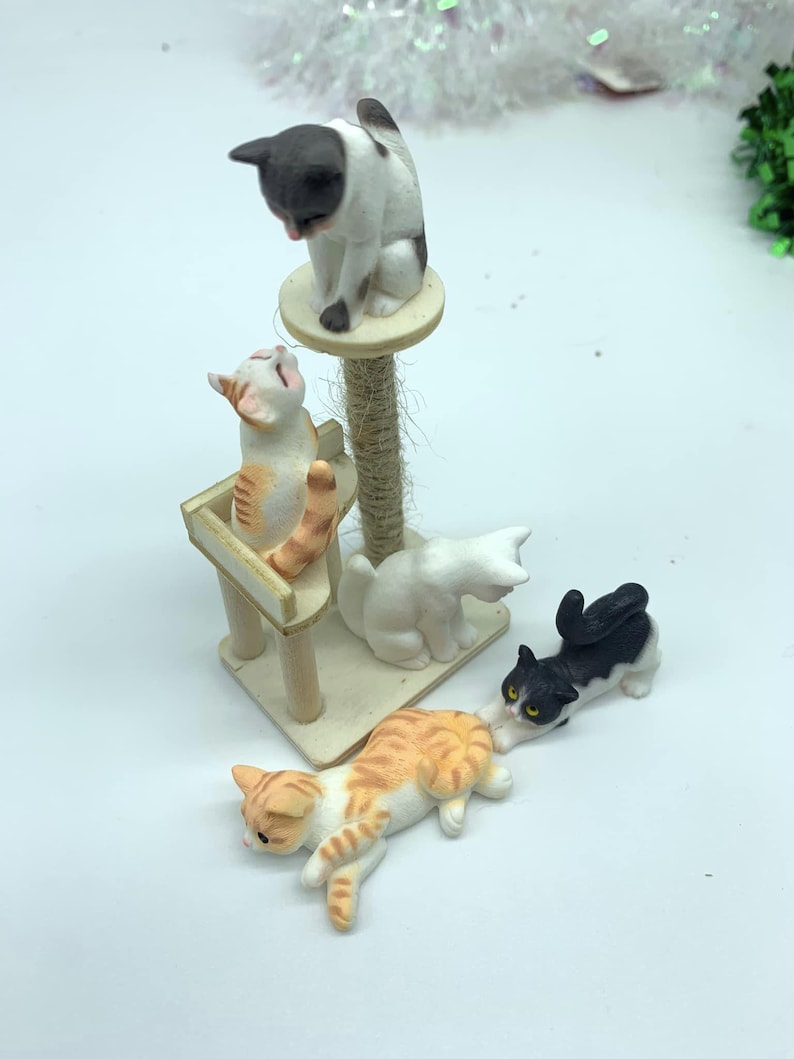 May include: A set of four miniature cat figurines, including a white cat with black spots, a black cat with white spots, a white cat with orange spots, and an orange cat with white spots. The cats are posed in various playful positions, including one cat climbing a miniature cat tree.