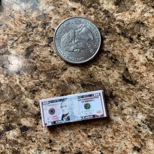 Może przedstawiać: Stos dziesięciu banknot&oacute;w dziesięciodolarowych z portretem Aleksandra Hamiltona na awersie. Banknoty są złożone na p&oacute;ł i zabezpieczone gumką. Banknoty leżą na brązowo-białej powierzchni w kropki.