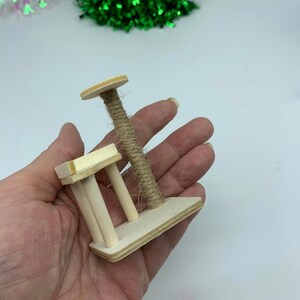 May include: A miniature wooden cat scratching post with a sisal rope scratching post and a small platform. The scratching post is held in a person's hand.