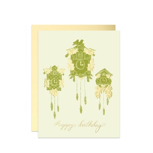 May include: A green and gold birthday card with three cuckoo clocks and the text "happy birthday".