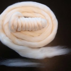 May include: A white, fluffy ball of wool yarn is rolled up and ready for knitting or crocheting.