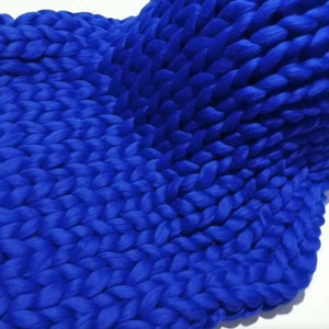 May include: A close-up of a chunky knit blanket in a vibrant blue colour. The blanket is made of thick yarn and has a soft, textured surface.