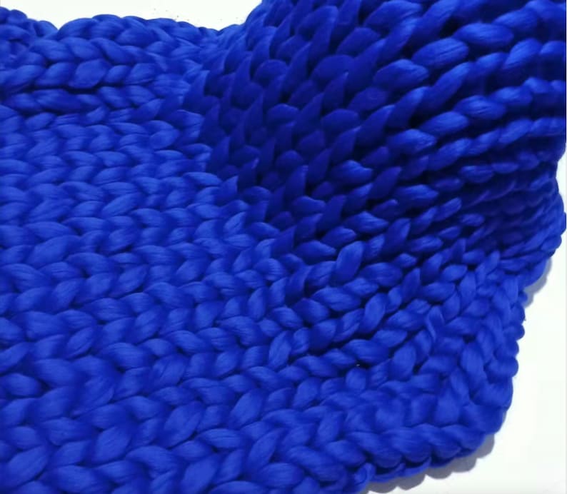 May include: A close-up of a chunky knit blanket in a vibrant blue colour. The blanket is made of thick yarn and has a soft, textured surface.
