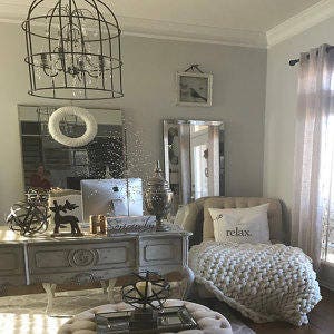 May include: A white, fluffy throw blanket with the word "relax" printed on it is draped over a white chaise lounge chair. The chair is in a room with a white desk, a mirror, and a large, caged chandelier.