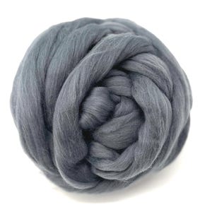 May include: A ball of gray roving yarn, tightly wound and textured. The wool fibers are a solid, muted gray color, and the yarn is displayed against a clean white background. Ideal for various fiber art projects.