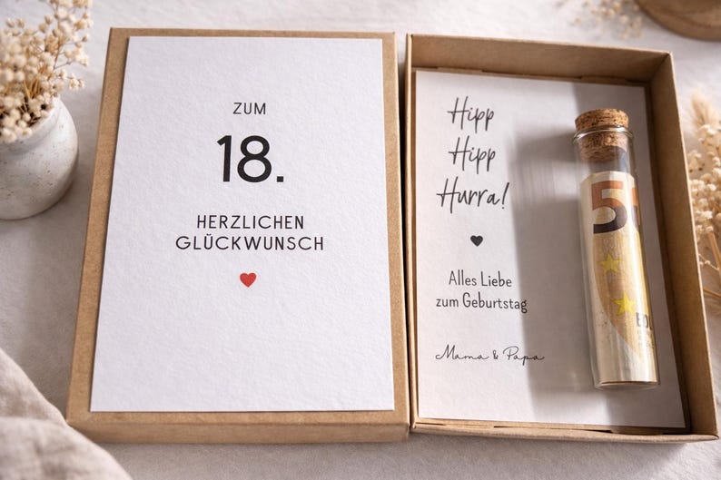 以下が含まれることがあります： 「ZUM 18. HERZLICHEN GL&Uuml;CKWUNSCH」と赤いハートのカードが入ったギフトボックス。内側には「Hipp Hipp Hurra！」と紙幣が入ったガラス管が入ったカードが入っています。
