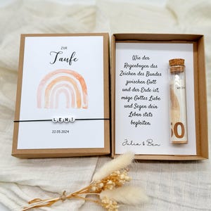 Pode incluir: Uma caixa de presente marrom com um cart&atilde;o branco que diz "Zur Taufe Leni 22.05.2024" e um arco-&iacute;ris de aquarela. O cart&atilde;o est&aacute; em uma caixa marrom com um cart&atilde;o branco que diz "Wie der Regenbogen das Zeichen des Bundes zwischen Gott und der Erde ist, moge Gottes Liebe und Segen dein Leben stets begleiten. Julia & Ben" e um frasco de vidro com uma nota dobrada dentro.
