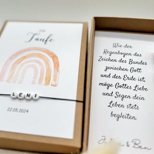 Pode incluir: Um cart&atilde;o branco com um arco-&iacute;ris de aquarela e o texto "Taufe" e "LENI" com a data "22.05.2024". O cart&atilde;o est&aacute; em uma caixa marrom com um cart&atilde;o branco dentro que tem texto sobre um arco-&iacute;ris como sinal do amor e da b&ecirc;n&ccedil;&atilde;o de Deus. Um pequeno frasco de vidro com um peda&ccedil;o de papel enrolado dentro tamb&eacute;m est&aacute; na caixa.