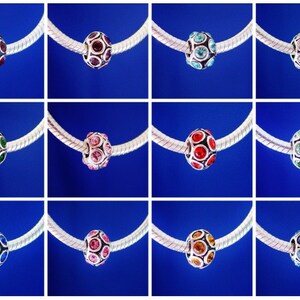 May include: Twelve silver charm beads with different colored crystal accents. Each bead is round and has a silver metal base with a pattern of small circles. The beads are displayed on a silver chain.