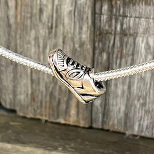 May include: A silver charm in the shape of a sneaker. The charm is detailed with a textured design and is attached to a silver chain.