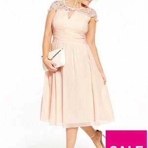 May include: A blush-colored knee-length dress with a pleated bodice and a keyhole neckline. The dress features cap sleeves with beaded embellishments and a wrapped waist. A white clutch and silver heels complete the look. The image includes a pink "SALE" graphic.