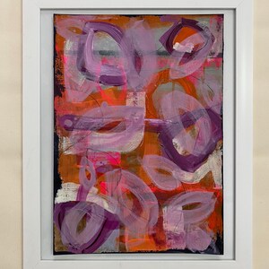May include: Abstract painting with a mix of pink, purple, orange, and white paint. The painting has a textured look and is framed in a white frame.