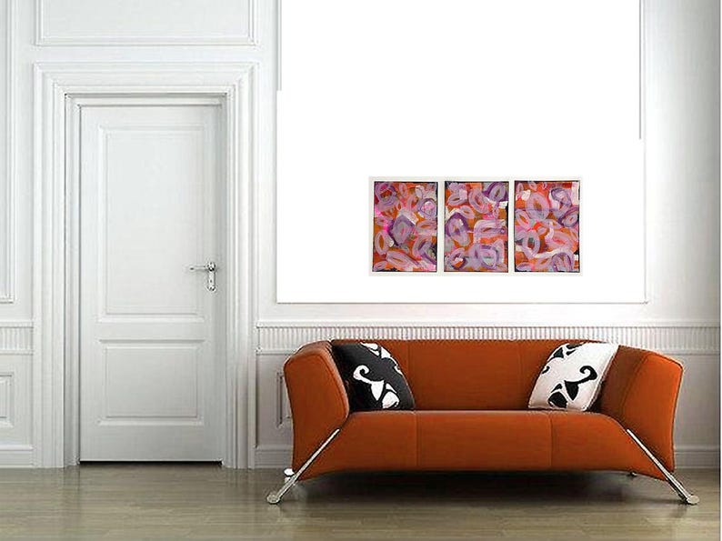 May include: Three abstract paintings with pink, orange, and purple swirls. The paintings are framed and hung on a white wall above a brown couch with black and white pillows.