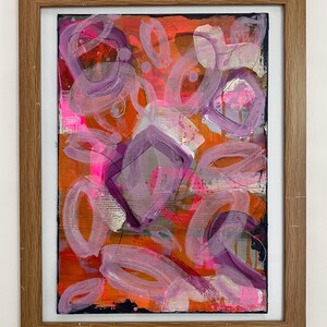 May include: Abstract painting with a bright orange background and purple and pink shapes. The painting is framed in a natural wood frame.