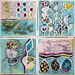 May include: Four square ceramic tiles with abstract floral designs. Each tile features a different design in shades of pink, blue, yellow, and white. The designs include stylized flowers, hearts, and geometric shapes.